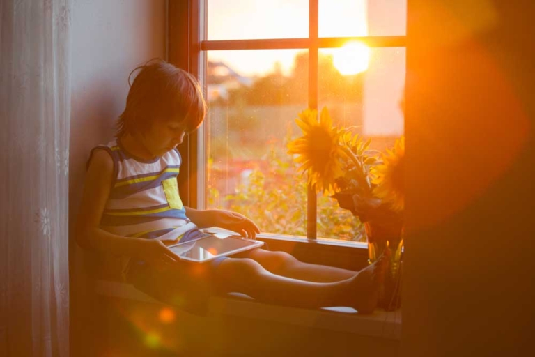 young boy sitting next to nook window with sun shining in