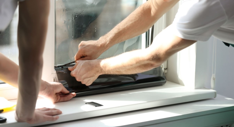 Two men apply window tint to a window in a home.